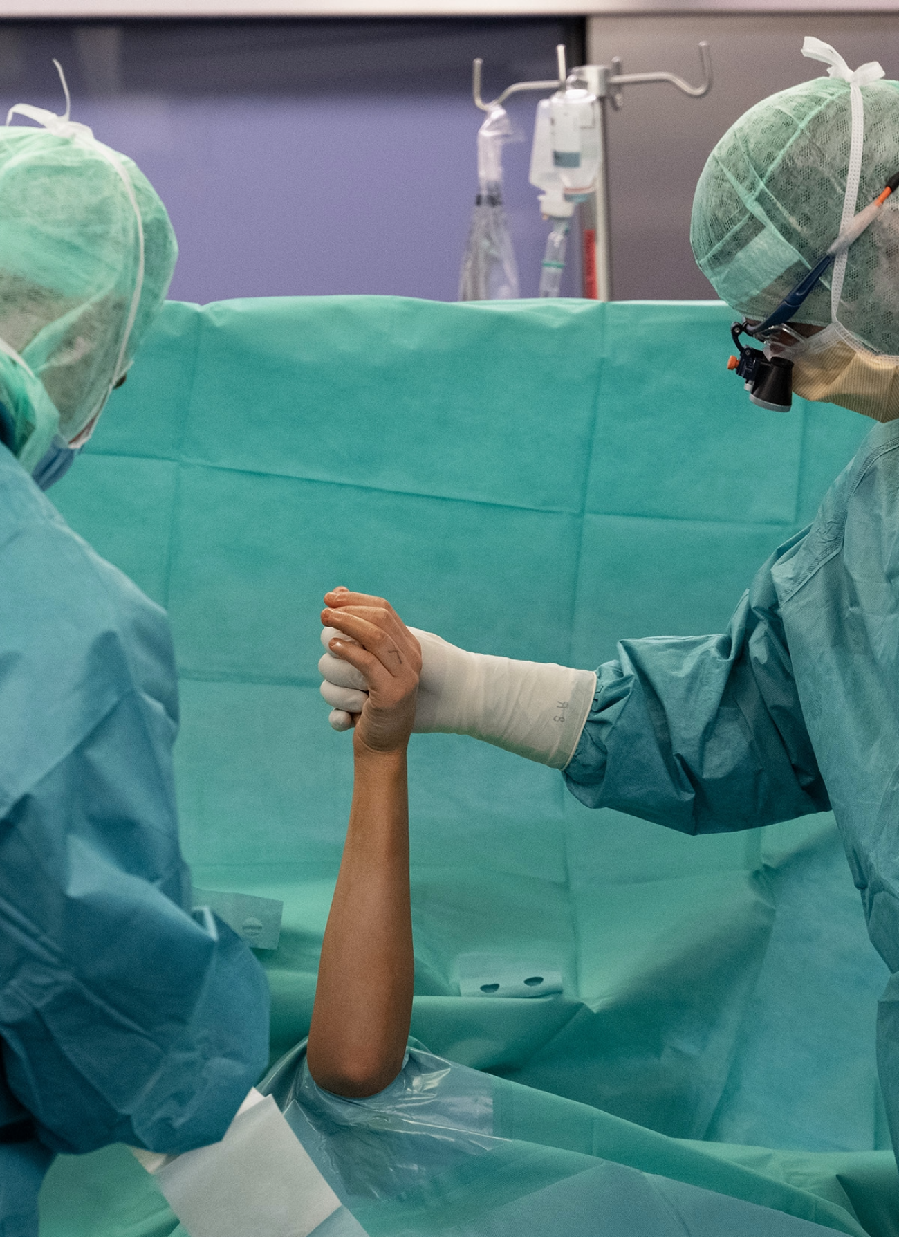 Zwei Ärzte im OP-Saal halten die Hand eines Patienten