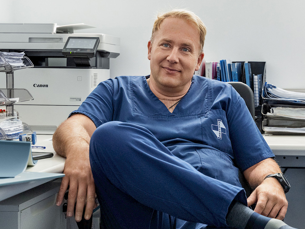 Portrait of Victor Costache in his office, a male doctor wearing blue surgical attire and blond hair